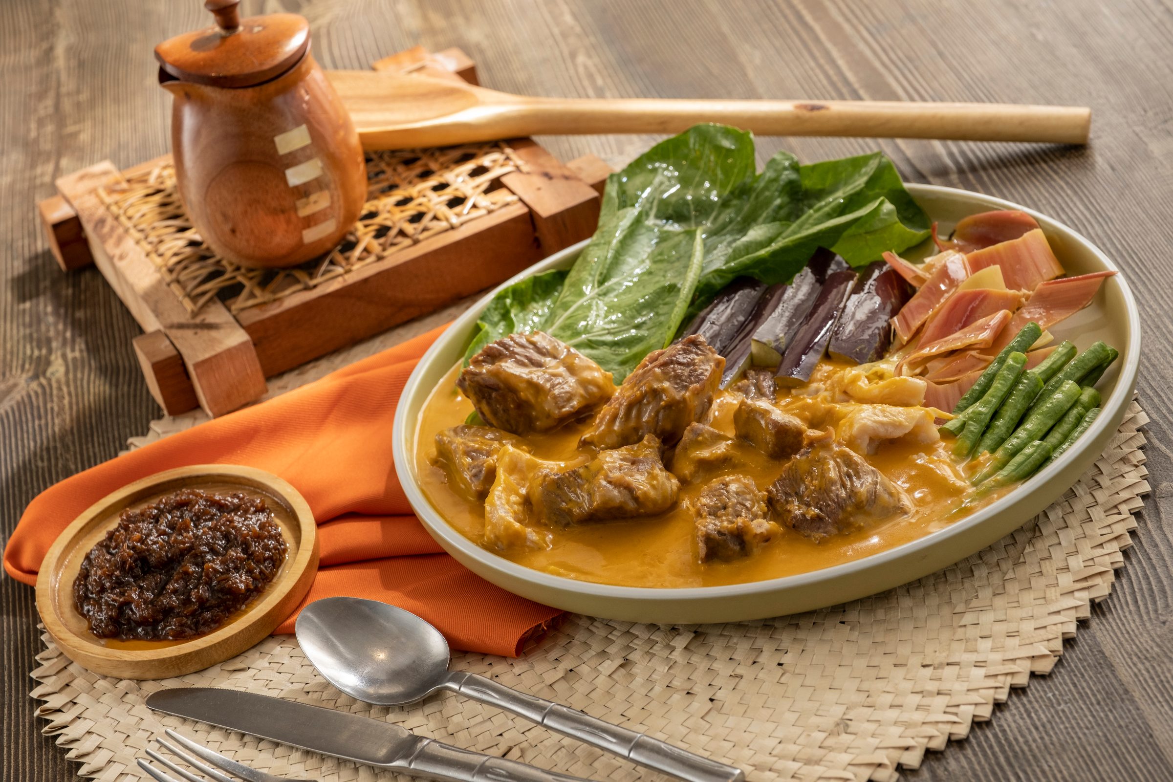 Kare-kare beef and tripe in peanut sauce with bok choy, eggplant, string beans and banana heart, with bagoong on the side, on a woven mat
